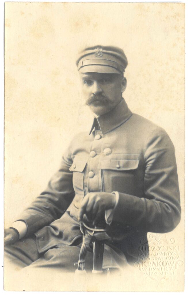 Fotografia czarno-biała, portret atelierowy przedstawiająca mężczyznę w wojskowym mundurze z szablą i rogatywką na głowie